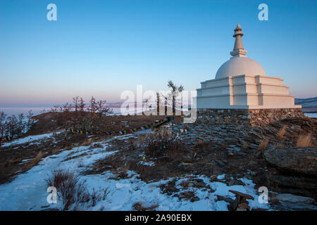 Stupa bouddhiste sur l'île de Ogoy sur le Lac Baïkal sur fond de ciel bleu en hiver. Près de l'aide d'un des drapeaux colorés sur les cordes. Neige sur le grou Banque D'Images