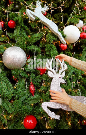 Vertical Image de Woman's Hands Glitter Décoration ornement de forme de rennes sur l'arbre de Noël Banque D'Images