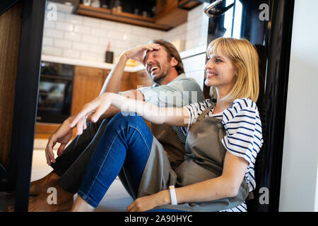 Les jeunes professionnels fatigué couple sitting on plancher de la cuisine après la cuisson Banque D'Images