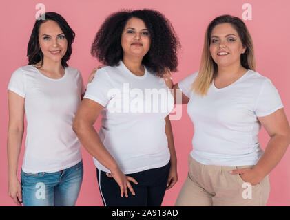 Trois copines sourire magnifiquement et pose devant l'appareil photo sur un fond rose. In White T-shirts. Conception de modèles pour Banque D'Images