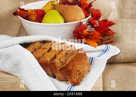 Des tranches de pain d'épices poire enveloppés dans des serviettes de cuisine blanche neuve propre. Les poires fraîches et les pommes sont dans un bol en céramique blanc entouré par des feuilles Banque D'Images