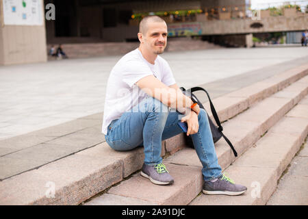 Homme assis sur des escaliers dans le parc avec sac à dos derrière lui Banque D'Images