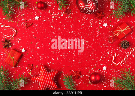 Noël ou bonne année la composition. Cadre fait de branches de sapin, des pommes de pin et des décorations de Noël sur fond rouge couverte de neige. Télévision. Banque D'Images