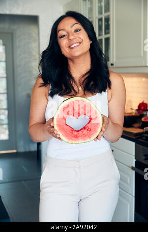 Woman in kitchen holding watermelon Banque D'Images