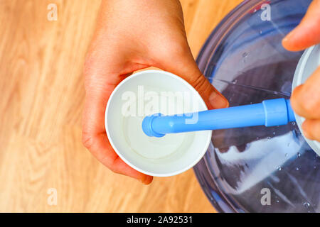 Femme mains verser de l'eau dans la tasse de papier à partir de la bouteille avec pompe à eau. Vue d'en haut. Banque D'Images