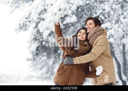 Cheerful Couple prenant sur Smartphone Selfies debout dans la forêt enneigée Banque D'Images