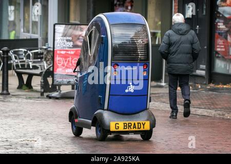 Un homme âgé entraîne une mobilité Shoprider clos et imperméable scooter sur le trottoir dans le centre-ville de Preston. Banque D'Images