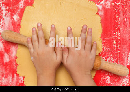 Les mains d'enfants rouler la pâte à biscuits de Noël. Banque D'Images