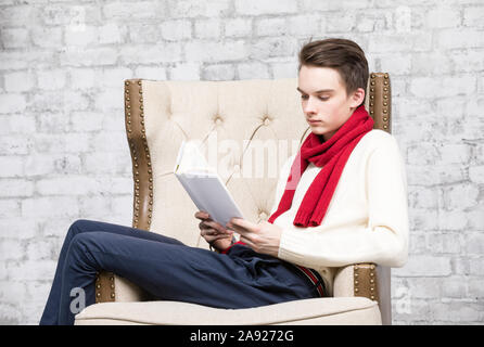 Adolescents portant foulard rouge et blanc pour homme assis dans un fauteuil à la maison Lire un livre Banque D'Images