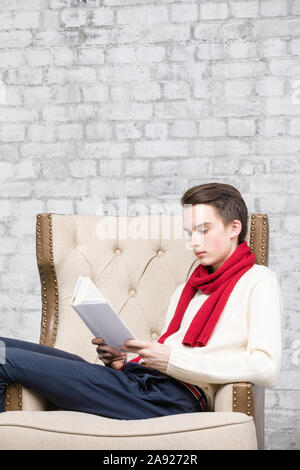 Adolescents portant foulard rouge et blanc pour homme assis dans un fauteuil à la maison Lire un livre Banque D'Images