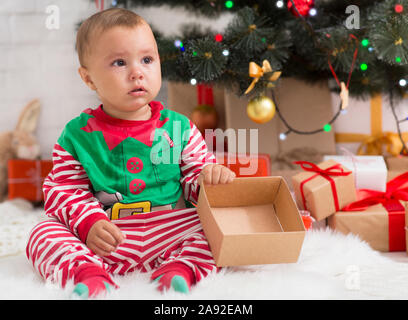 Bébé elfe malheureux avec vide présent fort assis près de l'arbre de Noël Banque D'Images