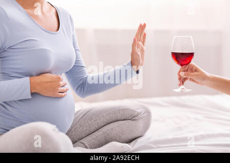 Méconnaissable fille enceinte refusant de prendre Wine Sitting on Bed Banque D'Images