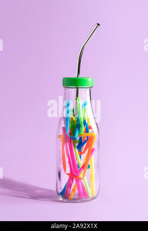 Réduire la pollution plastique concept avec une paille en métal réutilisable dans une bouteille en verre pleine de plastique colorés, sur papier violet. Eco-friendly paille. Banque D'Images