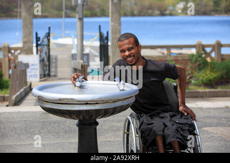 Homme qui a eu la méningite spinale dans un fauteuil roulant de boire de une fontaine Banque D'Images