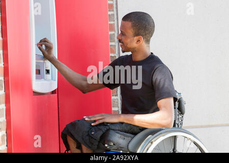 Homme qui avait une méningite spinale dans un fauteuil roulant à un banque ATM Banque D'Images