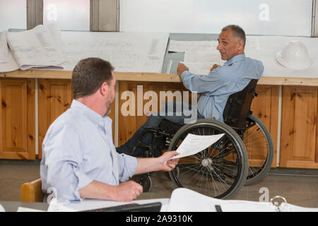 Deux ingénieurs de projet font de la paperasserie sur le travail, un en fauteuil roulant avec une blessure à la moelle épinière Banque D'Images