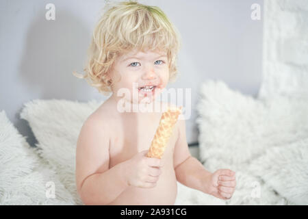 Petit enfant prenant gaufre et le manger avec plaisir et l'amusement sur arrière-plan de la salle blanche. Banque D'Images