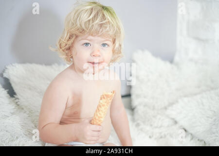 Petit enfant prenant gaufre et le manger avec plaisir et l'amusement sur arrière-plan de la salle blanche. Banque D'Images