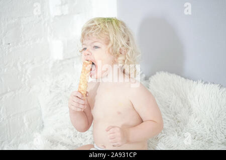 Petit enfant prenant gaufre et le manger avec plaisir et l'amusement sur arrière-plan de la salle blanche. Banque D'Images