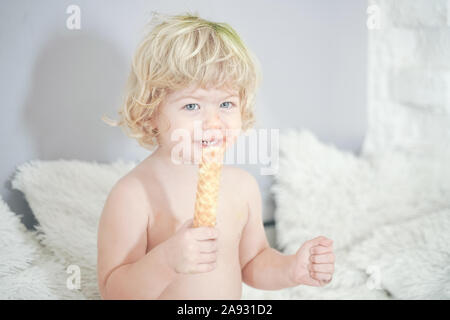 Petit enfant prenant gaufre et le manger avec plaisir et l'amusement sur arrière-plan de la salle blanche. Banque D'Images