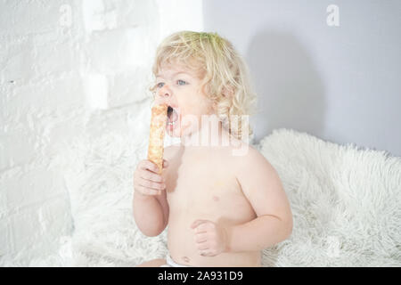 Petit enfant prenant gaufre et le manger avec plaisir et l'amusement sur arrière-plan de la salle blanche. Banque D'Images