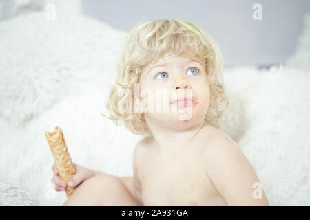 Petit enfant prenant gaufre et le manger avec plaisir et l'amusement sur arrière-plan de la salle blanche. Banque D'Images