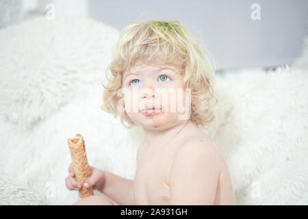 Petit enfant prenant gaufre et le manger avec plaisir et l'amusement sur arrière-plan de la salle blanche. Banque D'Images