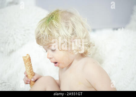 Petit enfant prenant gaufre et le manger avec plaisir et l'amusement sur arrière-plan de la salle blanche. Banque D'Images