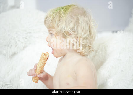 Petit enfant prenant gaufre et le manger avec plaisir et l'amusement sur arrière-plan de la salle blanche. Banque D'Images