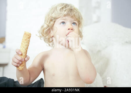 Petit enfant prenant gaufre et le manger avec plaisir et l'amusement sur arrière-plan de la salle blanche. Banque D'Images