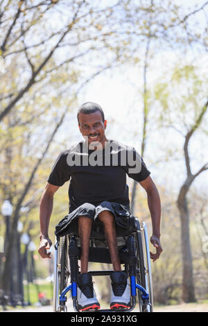 Homme dans un fauteuil roulant qui a eu la méningite spinale à travers un parc Banque D'Images