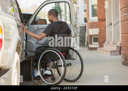Homme dans un fauteuil roulant qui a eu la méningite spinale entrant dans son véhicule accessible Banque D'Images