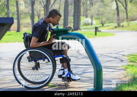 Homme en fauteuil roulant qui avait une méningite spinale à l'aide d'un fontaine publique Banque D'Images