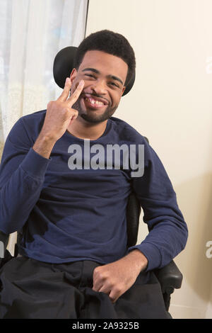 Portrait d'un homme afro-américain heureux avec paralysie cérébrale gestante en fauteuil roulant à la maison Banque D'Images