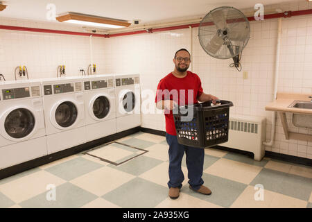 Homme afro-américain avec le syndrome de Down tenant le panier à linge dedans buanderie Banque D'Images