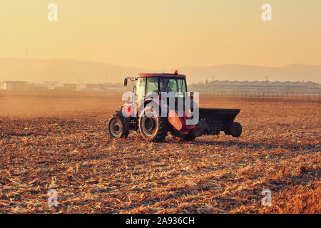 Coucher de soleil rouge tracteur moderne re cultive du chaume après la récolte de maïs d'automne par paillage, Brume de poussière à l'horizon Banque D'Images