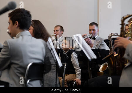 Kiev - nov, 10, 2019 : un petit garçon est assis dans un orchestre près les musiciens jouent divers instruments de musique en costumes gris. Banque D'Images