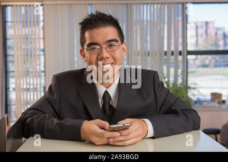 Portrait d'un homme asiatique heureux avec l'autisme à l'aide de son téléphone dans un bureau Banque D'Images