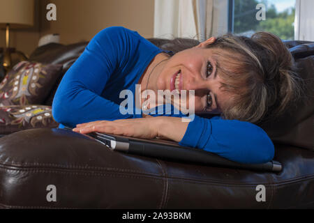 Femme avec une déficience visuelle couchée et souriante sur elle ordinateur dans la salle de séjour Banque D'Images