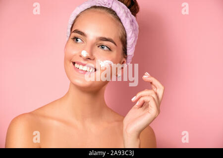 Une belle fille avec un bandage sur sa tête un fond rose avec des taches crème sur son visage Banque D'Images