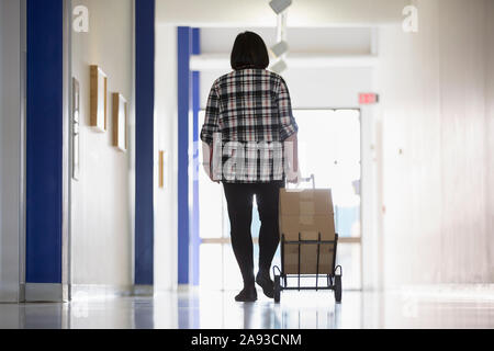 Femme asiatique ayant un handicap d'apprentissage qui prend des boîtes en bas d'un hall des bureaux Banque D'Images