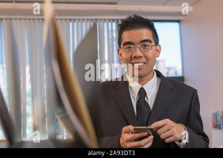 Homme asiatique avec l'autisme travaillant dans un bureau avec son téléphone Banque D'Images