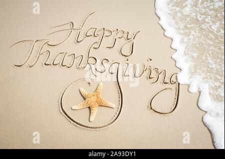 Message joyeux Thanksgiving à la main sur une plage de sable fin avec des étoiles de mer et de vague Banque D'Images