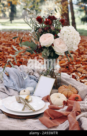 Table de mariage d'automne. Garden party fête, pique-nique avec golden couverts, assiette de porcelaine,verre de vin blanc et pumkins. Bouquet de fleurs rose Banque D'Images