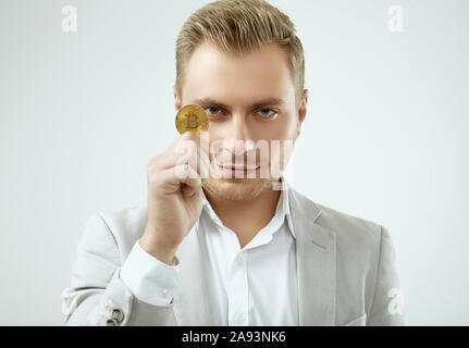 Portrait d'un bel homme blond modèle dans un costume gris de la mode est titulaire d'un Bitcoin isolé sur fond blanc en studio Banque D'Images