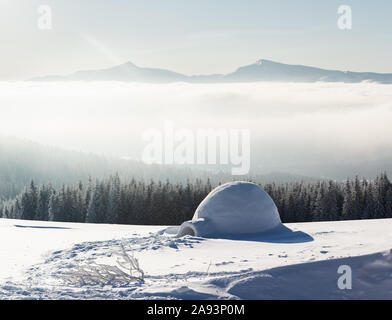 La vraie neige maison igloo en hiver montagnes des Carpates. Sapins couverts de neige et des pics de montagne dans le brouillard sur l'arrière-plan Banque D'Images