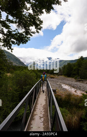 Jeune femme à traverser un pont métallique contre glacier du Mont Tronador en Pampa Linda, Parc National Nahuel Huapi, Patagonie, Argentine Banque D'Images