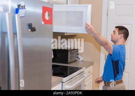 Homme avec le syndrome de Down ouvrant tiroir dans la cuisine Banque D'Images