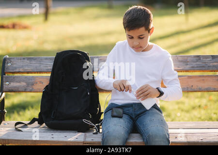 Teenage boy en chemise blanche utiliser powerbank pour charger son smartphone otside. Batterie faible sur smartphone Banque D'Images