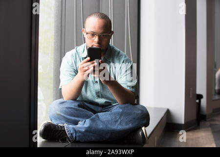 Homme afro-américain qui a le syndrome de Down à son regarder téléphone Banque D'Images